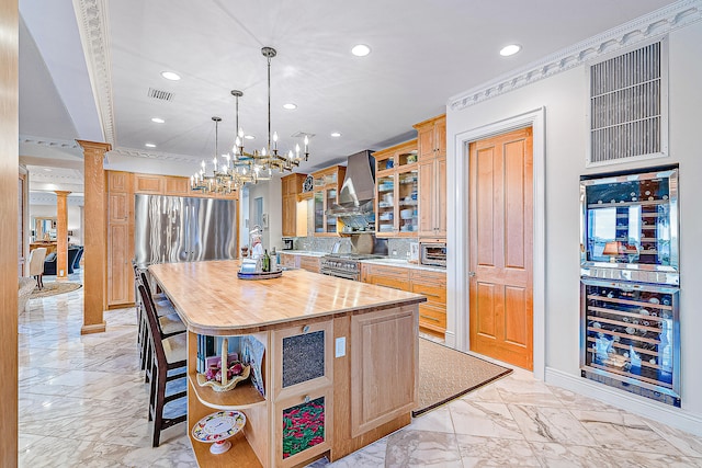 kitchen with appliances with stainless steel finishes, a kitchen island, a breakfast bar, wall chimney range hood, and decorative columns