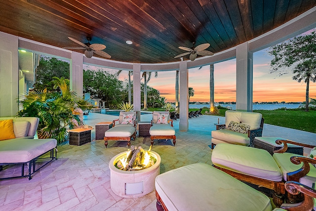 patio terrace at dusk featuring ceiling fan, a water view, and an outdoor living space with a fire pit