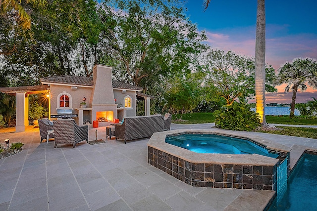 pool at dusk with exterior fireplace, area for grilling, an in ground hot tub, and a patio area