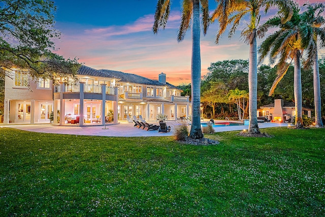 back house at dusk with a patio area, a yard, and a balcony