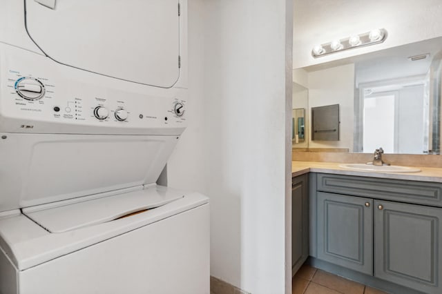 laundry room with light tile flooring, sink, and stacked washing maching and dryer