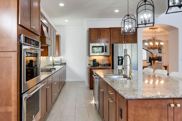 kitchen featuring stainless steel appliances, a center island with sink, decorative backsplash, hanging light fixtures, and sink