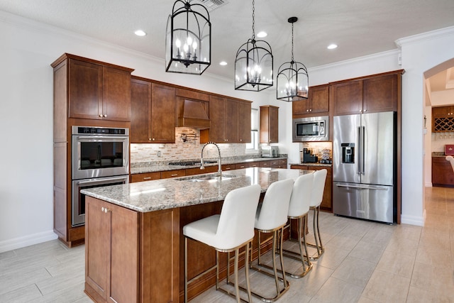 kitchen with stainless steel appliances, light stone counters, sink, a kitchen island with sink, and pendant lighting