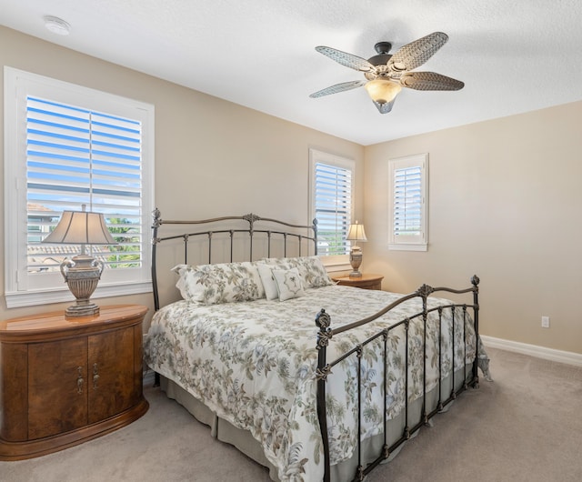 bedroom featuring a textured ceiling, light carpet, multiple windows, and ceiling fan