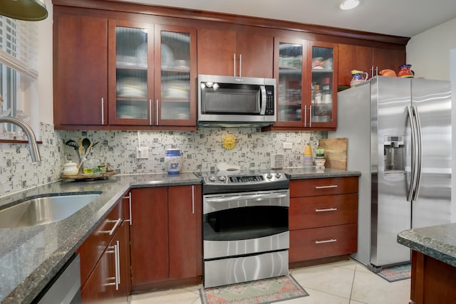 kitchen with tasteful backsplash, appliances with stainless steel finishes, light tile floors, and dark stone counters