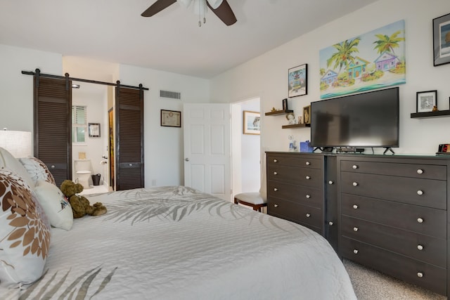 carpeted bedroom with a barn door, ensuite bathroom, and ceiling fan