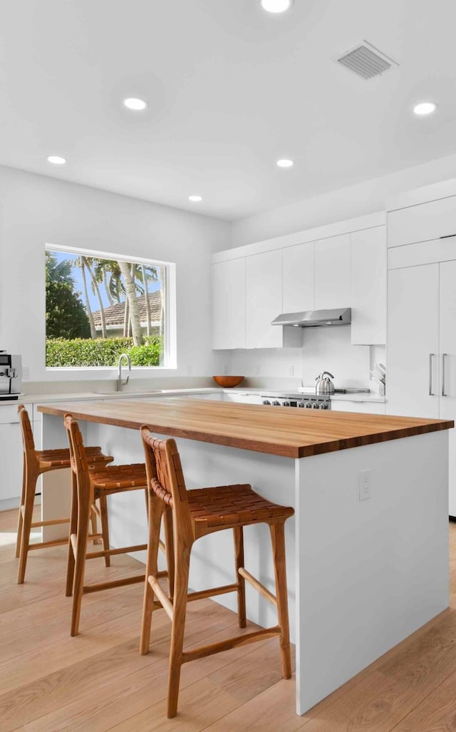 kitchen featuring butcher block counters, a breakfast bar, light hardwood / wood-style flooring, and white cabinetry