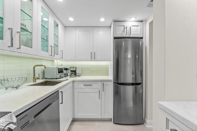 kitchen with sink, appliances with stainless steel finishes, light tile flooring, tasteful backsplash, and white cabinetry