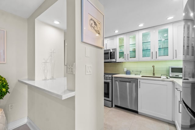 kitchen with sink, stainless steel appliances, light tile flooring, tasteful backsplash, and white cabinetry