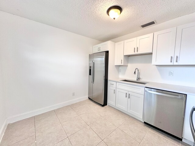 kitchen featuring appliances with stainless steel finishes, light tile flooring, a textured ceiling, white cabinetry, and sink