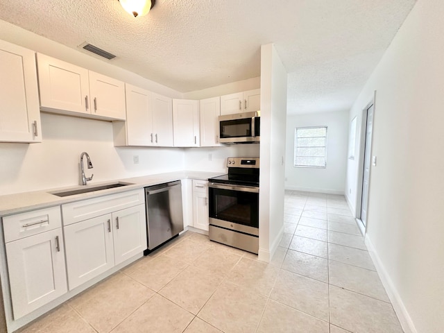 kitchen with sink, appliances with stainless steel finishes, light tile flooring, and white cabinetry