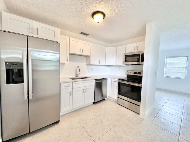 kitchen with light tile flooring, white cabinetry, appliances with stainless steel finishes, sink, and a textured ceiling