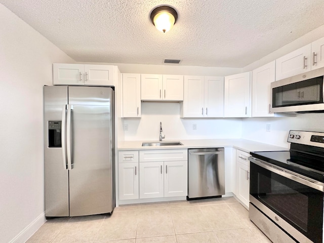 kitchen with white cabinets, light tile flooring, appliances with stainless steel finishes, sink, and a textured ceiling