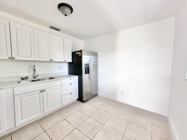 kitchen featuring a textured ceiling, white cabinets, sink, light tile flooring, and stainless steel fridge