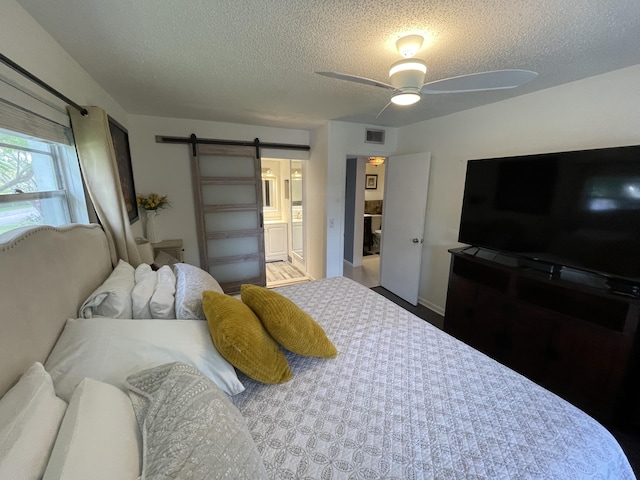 bedroom featuring a textured ceiling, a barn door, ensuite bathroom, and ceiling fan