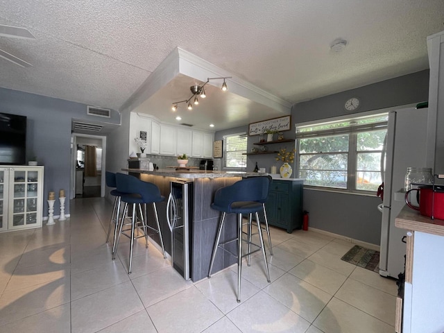 kitchen featuring kitchen peninsula, a breakfast bar, a textured ceiling, butcher block countertops, and white cabinetry