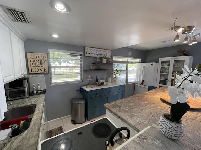 kitchen with white cabinets, white refrigerator, blue cabinets, sink, and light tile patterned floors