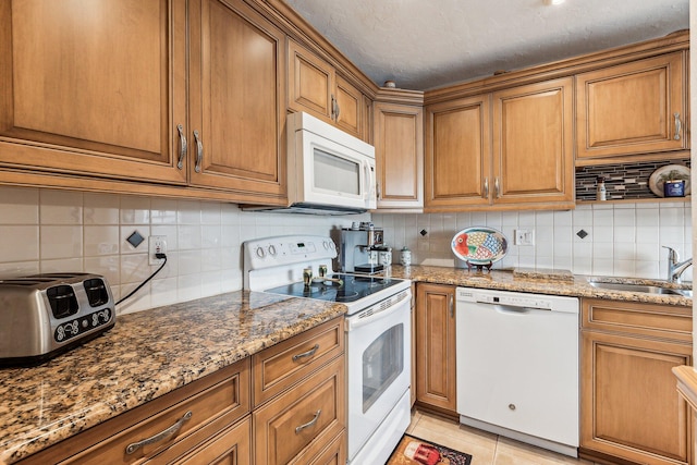 kitchen featuring light stone counters, tasteful backsplash, sink, white appliances, and light tile floors