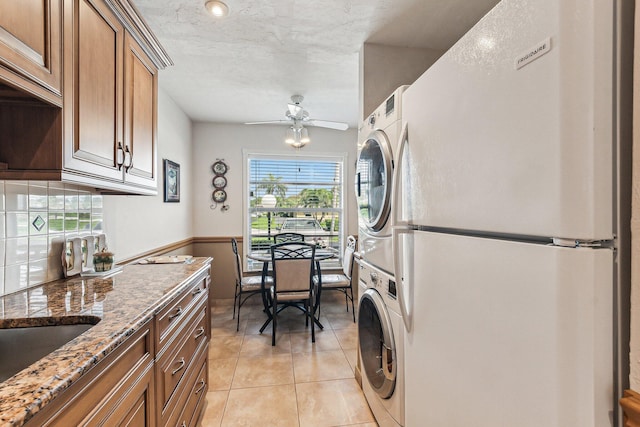 kitchen featuring stacked washer / dryer, light stone counters, white fridge, ceiling fan, and light tile floors