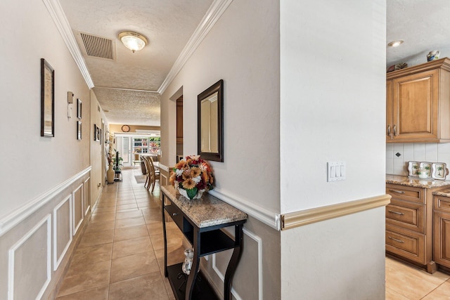 hallway with light tile floors, a textured ceiling, and crown molding