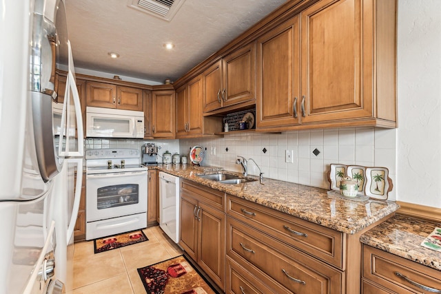 kitchen with light stone counters, backsplash, sink, white appliances, and light tile floors