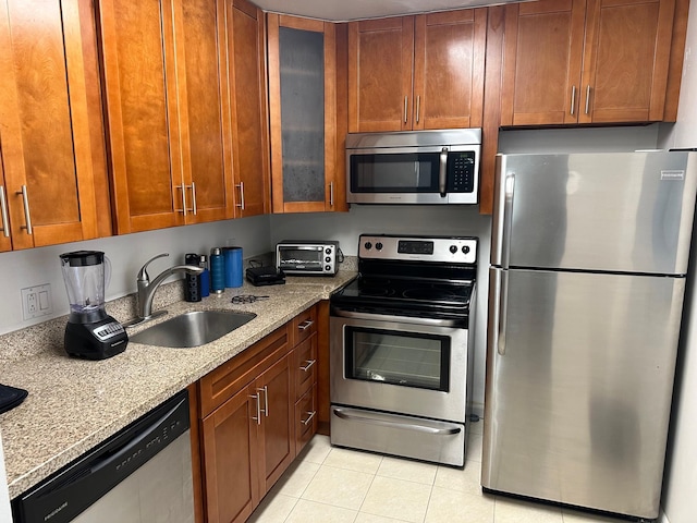 kitchen featuring light stone countertops, light tile patterned flooring, a sink, stainless steel appliances, and glass insert cabinets