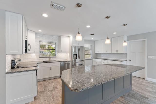 kitchen featuring white cabinetry, hanging light fixtures, a center island, light wood-type flooring, and stainless steel appliances