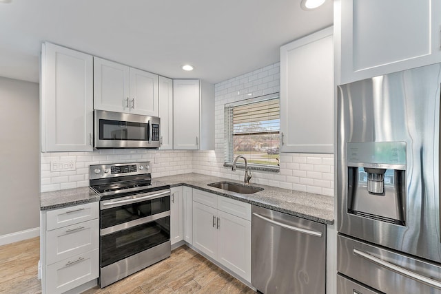 kitchen featuring white cabinetry, sink, light hardwood / wood-style flooring, dark stone countertops, and appliances with stainless steel finishes