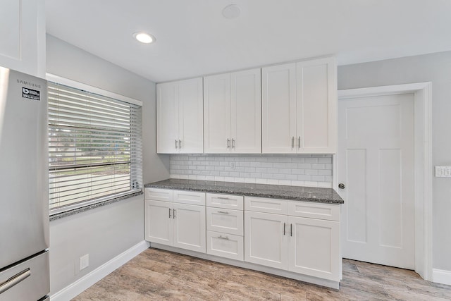 kitchen with white cabinetry, stainless steel refrigerator, backsplash, and dark stone countertops