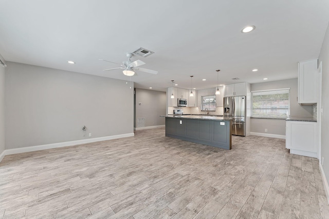 kitchen featuring white cabinetry, hanging light fixtures, appliances with stainless steel finishes, a kitchen island, and light wood-type flooring