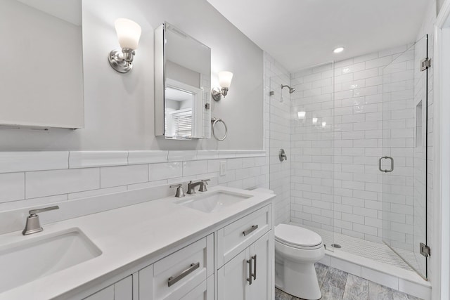 bathroom featuring vanity, toilet, tile walls, and a shower with door