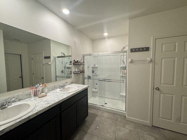 bathroom featuring a shower with door, a textured ceiling, double sink vanity, and tile flooring