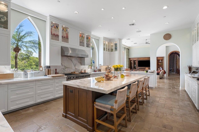 kitchen featuring tasteful backsplash, a center island, white cabinetry, and wall chimney range hood