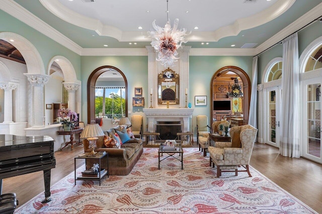 living room with decorative columns, a notable chandelier, light hardwood / wood-style flooring, a raised ceiling, and french doors