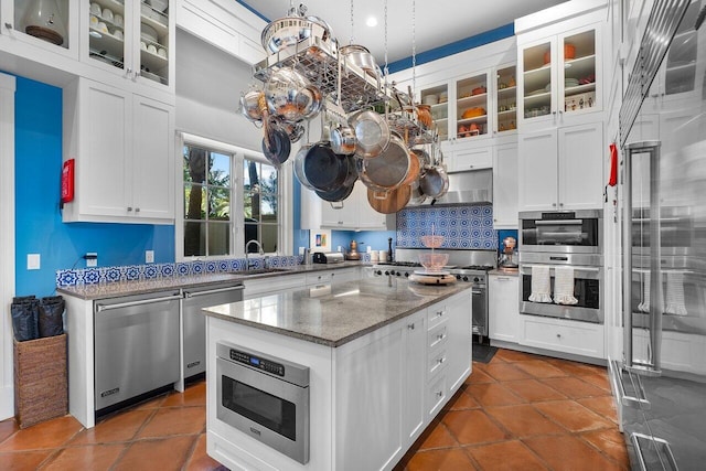 kitchen with appliances with stainless steel finishes, white cabinets, a center island, tasteful backsplash, and pendant lighting