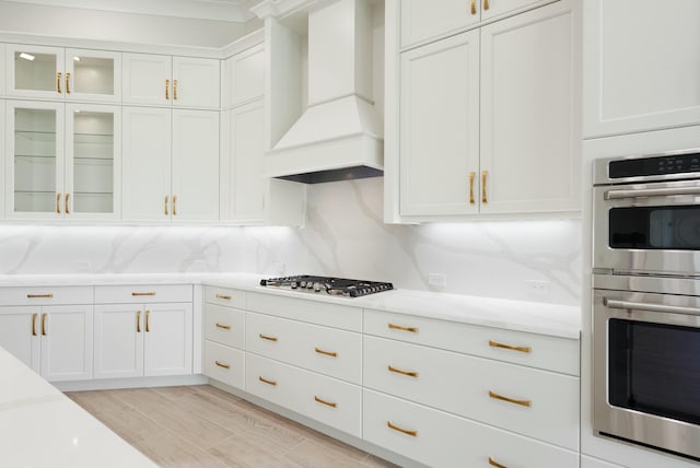 kitchen with custom range hood, white cabinetry, backsplash, and appliances with stainless steel finishes