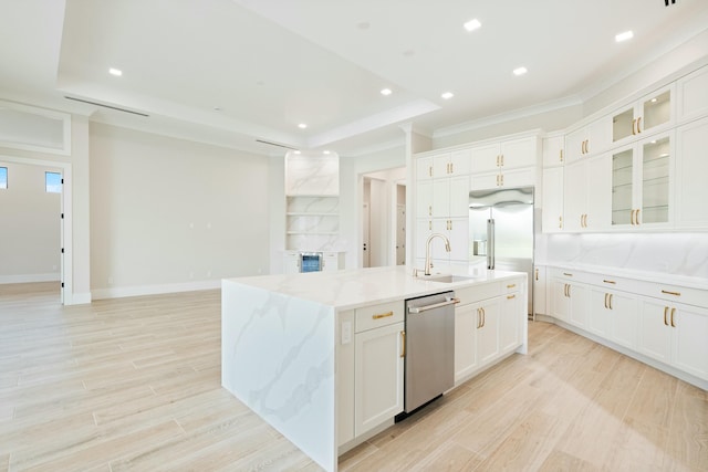 kitchen featuring white cabinetry, light stone counters, a raised ceiling, a center island with sink, and appliances with stainless steel finishes