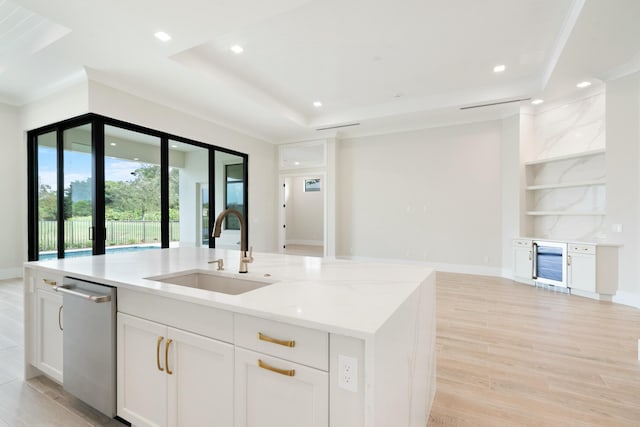 kitchen with beverage cooler, an island with sink, a tray ceiling, sink, and white cabinetry