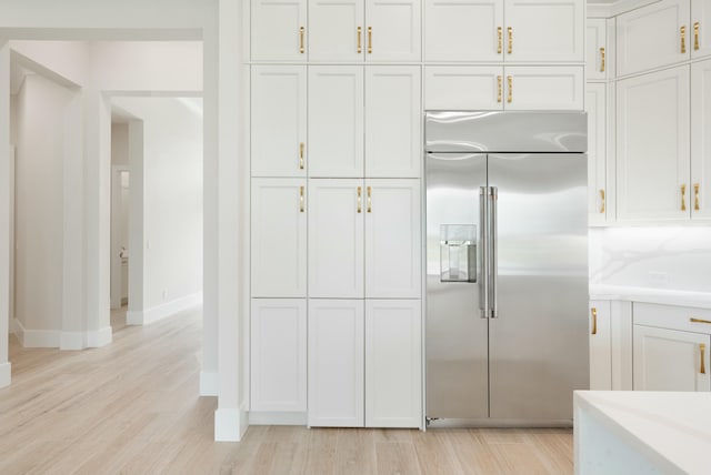 kitchen with stainless steel built in refrigerator, white cabinets, and light hardwood / wood-style flooring