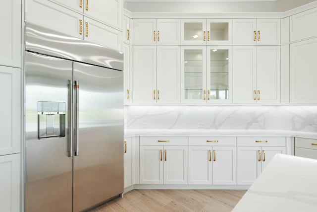 kitchen with stainless steel built in fridge, white cabinets, tasteful backsplash, and light stone countertops