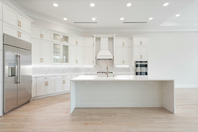 kitchen with stainless steel appliances, a center island with sink, custom exhaust hood, and white cabinetry