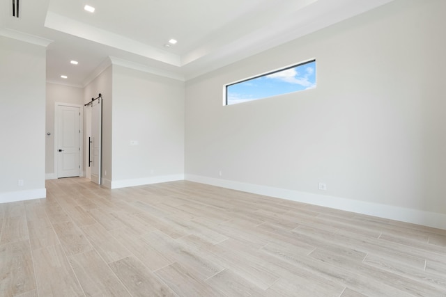 empty room featuring a raised ceiling, ornamental molding, a barn door, and light hardwood / wood-style flooring