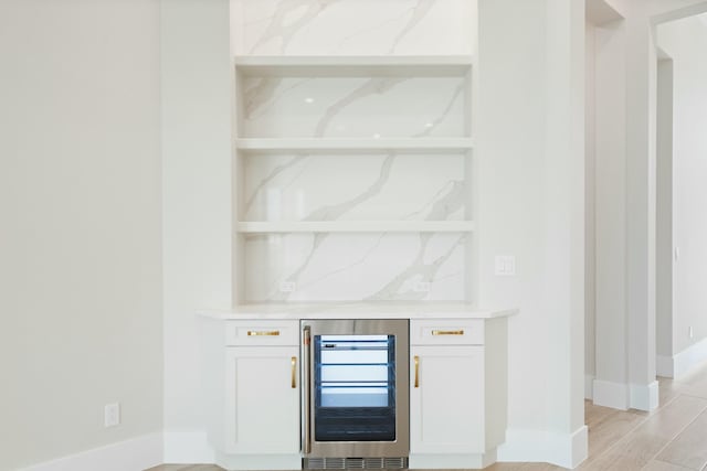 bar with light stone counters, white cabinets, beverage cooler, and light wood-type flooring