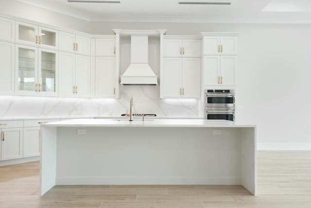 kitchen with white cabinetry, light wood-type flooring, stainless steel double oven, and custom range hood