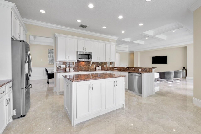 kitchen with coffered ceiling, white cabinetry, appliances with stainless steel finishes, dark stone counters, and a kitchen island