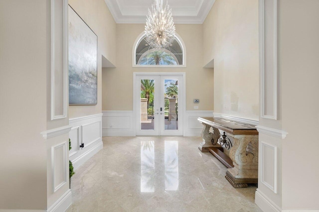 tiled foyer featuring crown molding, french doors, a chandelier, and a towering ceiling