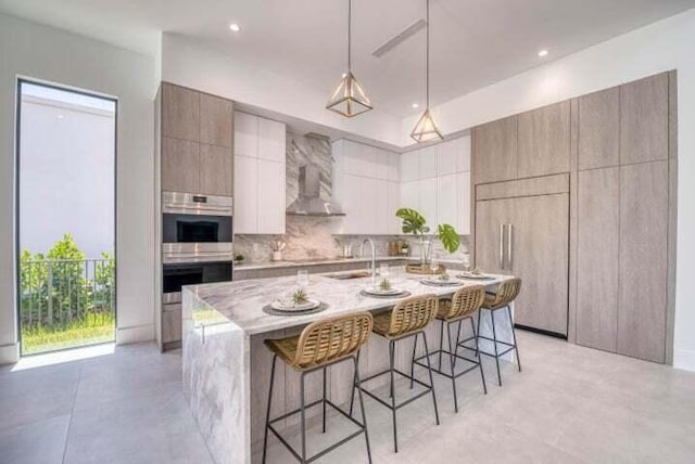 kitchen with an island with sink, a kitchen bar, double oven, sink, and extractor fan