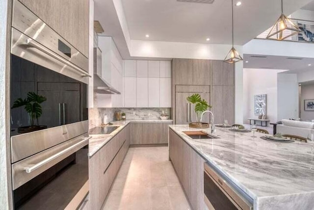 kitchen with sink, white cabinetry, stainless steel double oven, decorative light fixtures, and a spacious island