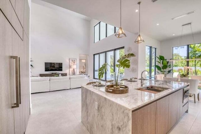 kitchen featuring light stone countertops, a center island with sink, sink, and plenty of natural light