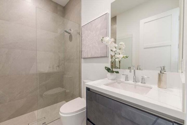 bathroom with a tile shower, vanity, and toilet